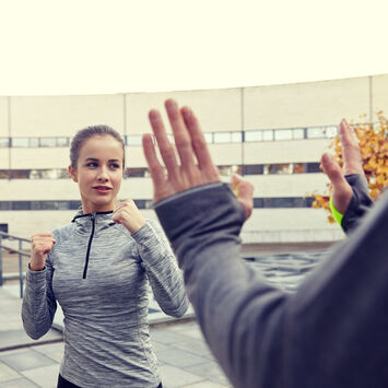 Frau in Sportkleidung übt Selbstverteidigung mit einem Partner im Freien