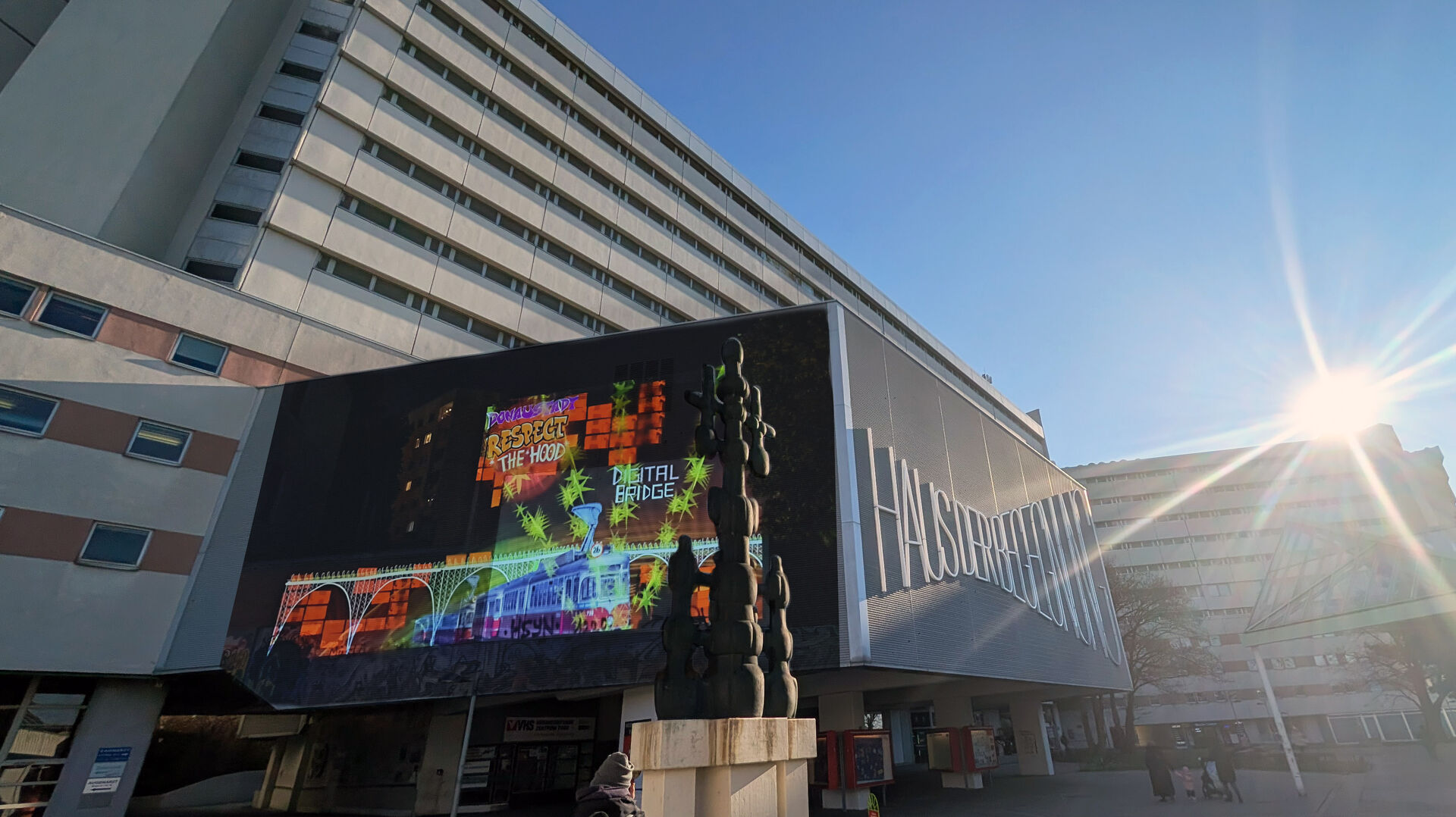 Großformatige, bunte Projektionen an der Fassade eines modernen Gebäudes im Wohnumfeld; die Installation ist in den urbanen Raum integriert.