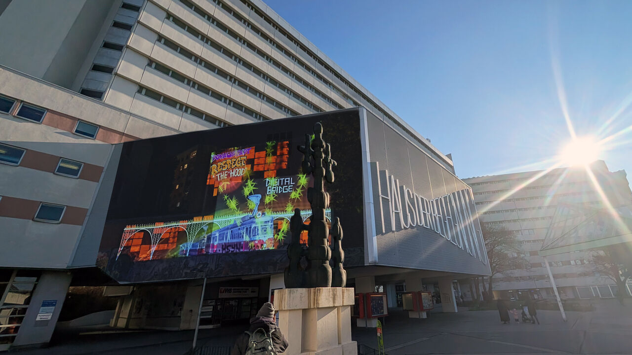 Großformatige, bunte Projektionen an der Fassade eines modernen Gebäudes im Wohnumfeld; die Installation ist in den urbanen Raum integriert.