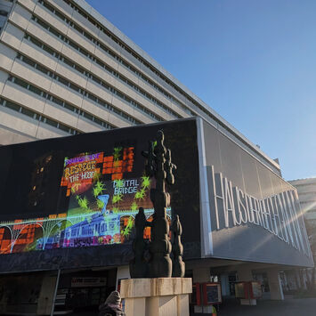 Großformatige, bunte Projektionen an der Fassade eines modernen Gebäudes im Wohnumfeld; die Installation ist in den urbanen Raum integriert.