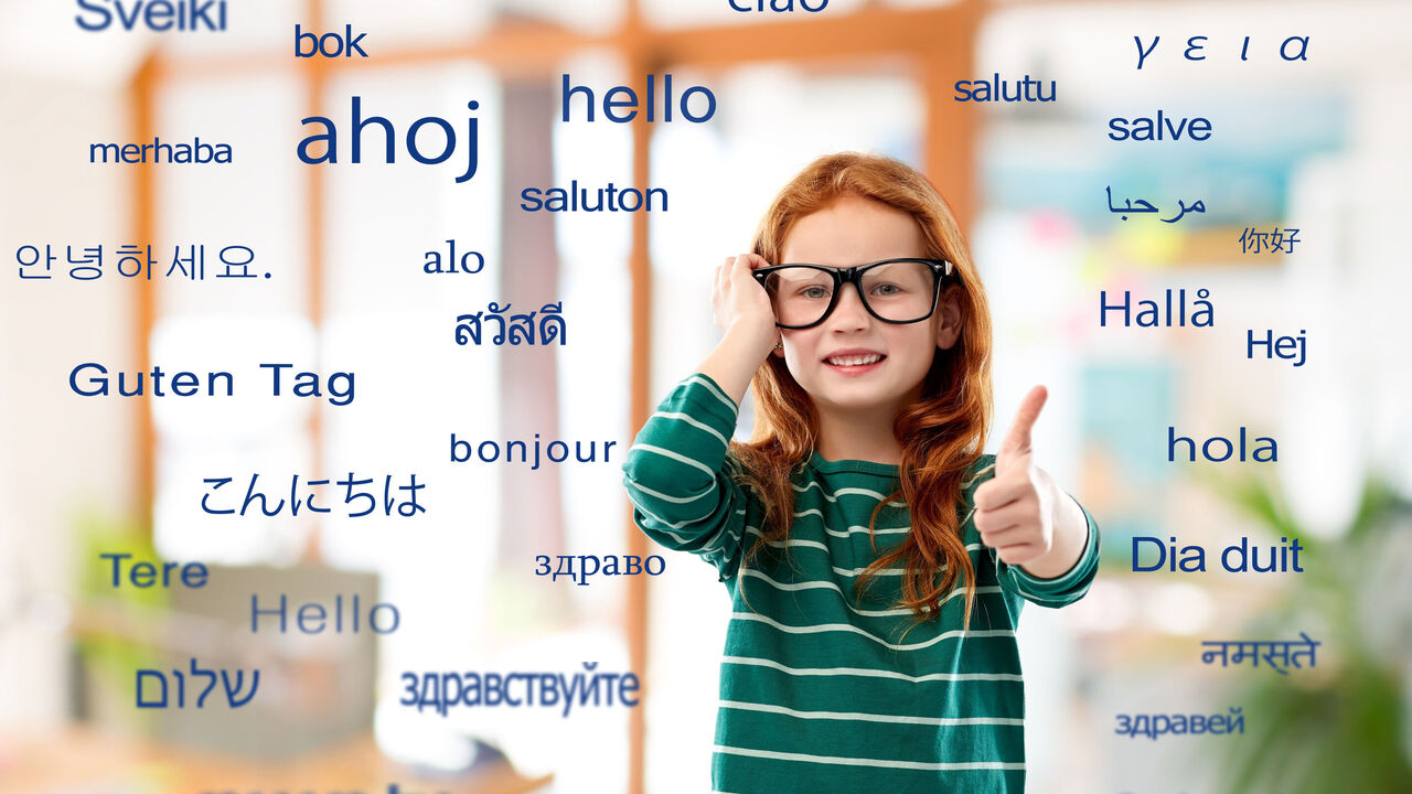 Ein rothaariges Mädchen setzt sich eine zu große Brille auf und hält einen Daumen hoch. Rund um sie steht "Guten Tag" in vielen verschiedenen Fremdsprachen.