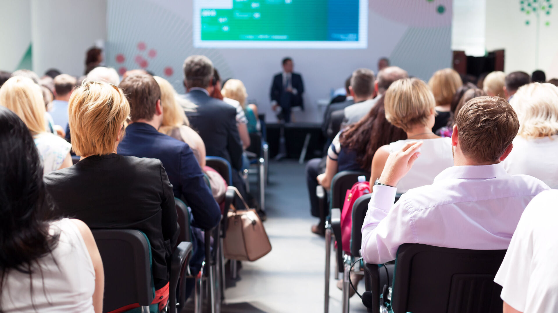 Menschen, die in einem Saal sitzen und einem Vortrag zuhören.