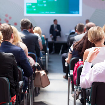 Menschen, die in einem Saal sitzen und einem Vortrag zuhören.