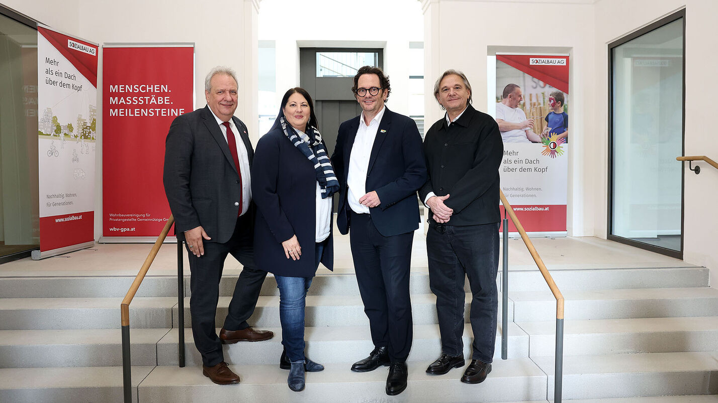 Drei Männer und eine Frau stehen auf Stufen in einem alten aber frischrenovierten Stiegenhaus.