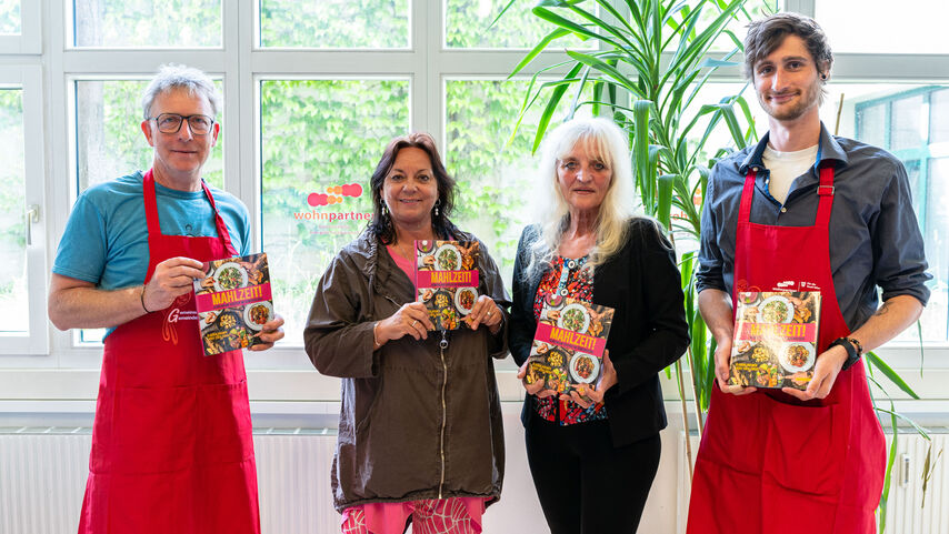 wohnpartner-Mitarbeiter*innen präsentieren stolz das neue Kochbuch. Jede*r hält ein Buch in Händen.