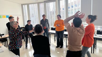 Einige Personen stehen im Kreis und werfen einander mehrere rote Bälle zu. Schulungs-/Workshopsituation