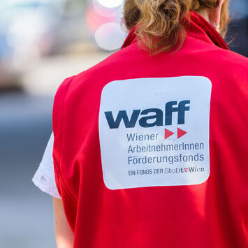 Rückenansicht einer Frau mit roter Weste mit der Aufschrift "waff Wiener ArbeitnehmerInnen Förderungsfonds"