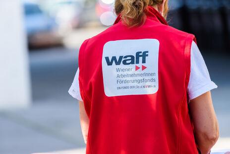 Rückenansicht einer Frau mit roter Weste mit der Aufschrift "waff Wiener ArbeitnehmerInnen Förderungsfonds"