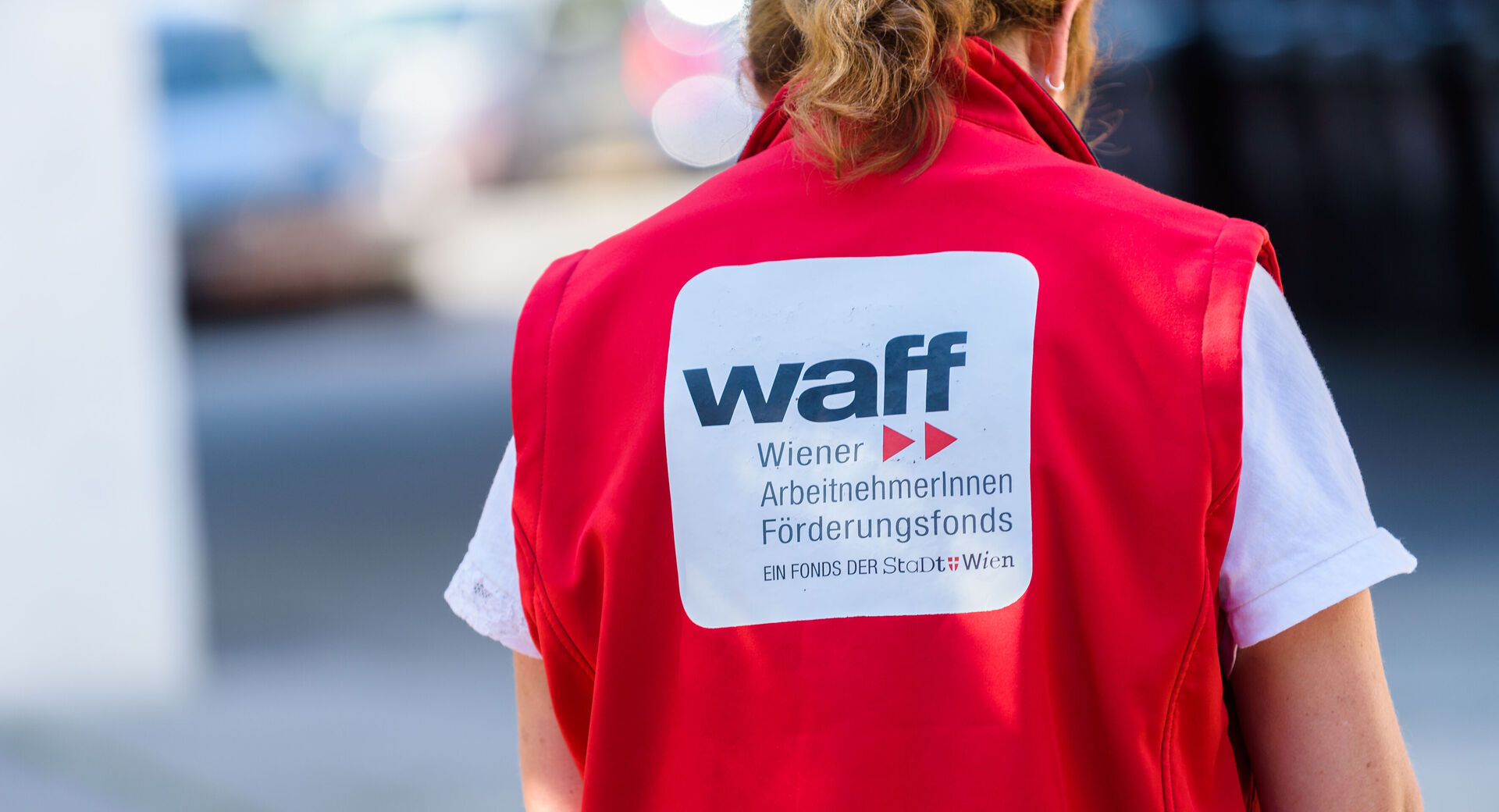 Rückenansicht einer Frau mit roter Weste mit der Aufschrift "waff Wiener ArbeitnehmerInnen Förderungsfonds"