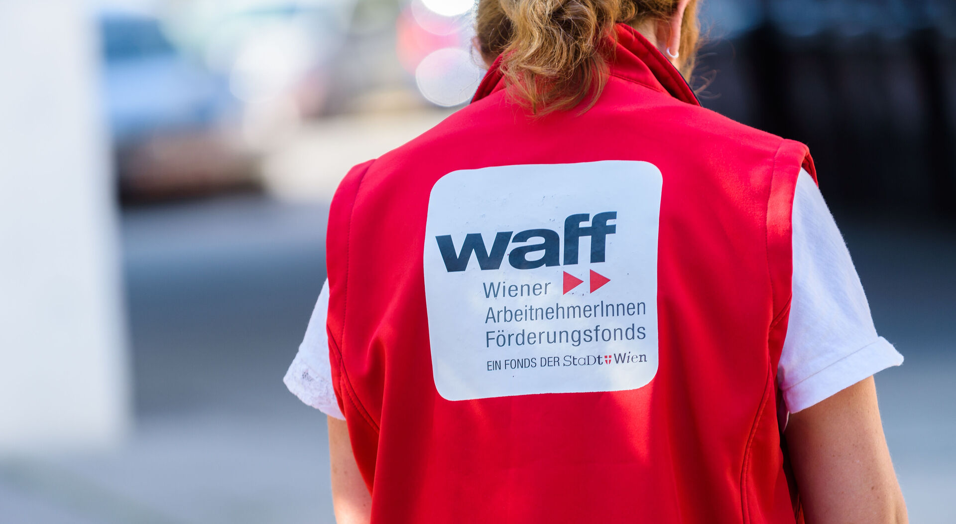 Rückenansicht einer Frau mit roter Weste mit der Aufschrift "waff Wiener ArbeitnehmerInnen Förderungsfonds"