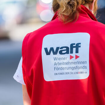 Rückenansicht einer Frau mit roter Weste mit der Aufschrift "waff Wiener ArbeitnehmerInnen Förderungsfonds"