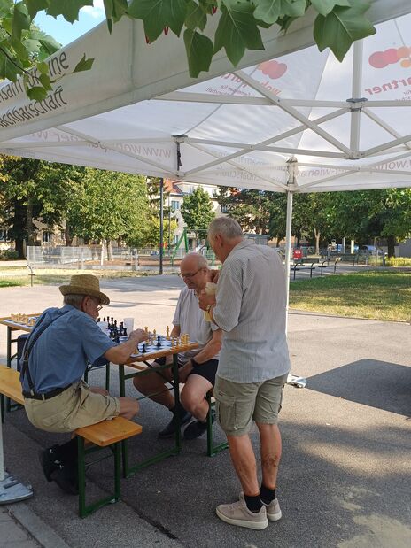 Drei ältere Männer spielen Schach an einem Tisch unter einem Pavillon im Freien