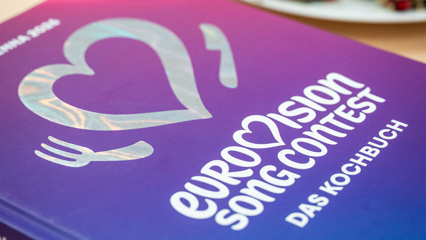 Kochbuch mit dem Titel 'EUROVISION SONG CONTEST - DAS KOCHBUCH' auf einem Tisch vor zwei Tellern mit gerollten Speisen