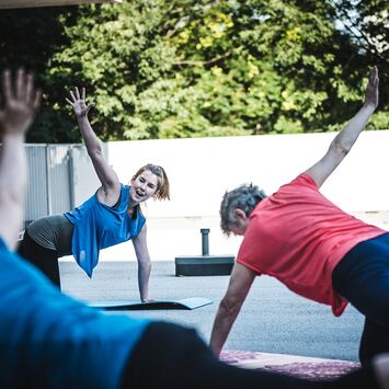 Eine Gruppe Frauen führen auf Gymnastikmatten am Boden Pilates-Übungen aus.