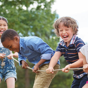 Vier Kinder, zwei Mädchen und zwei Jungs, ziehen lachend an einem Seil.