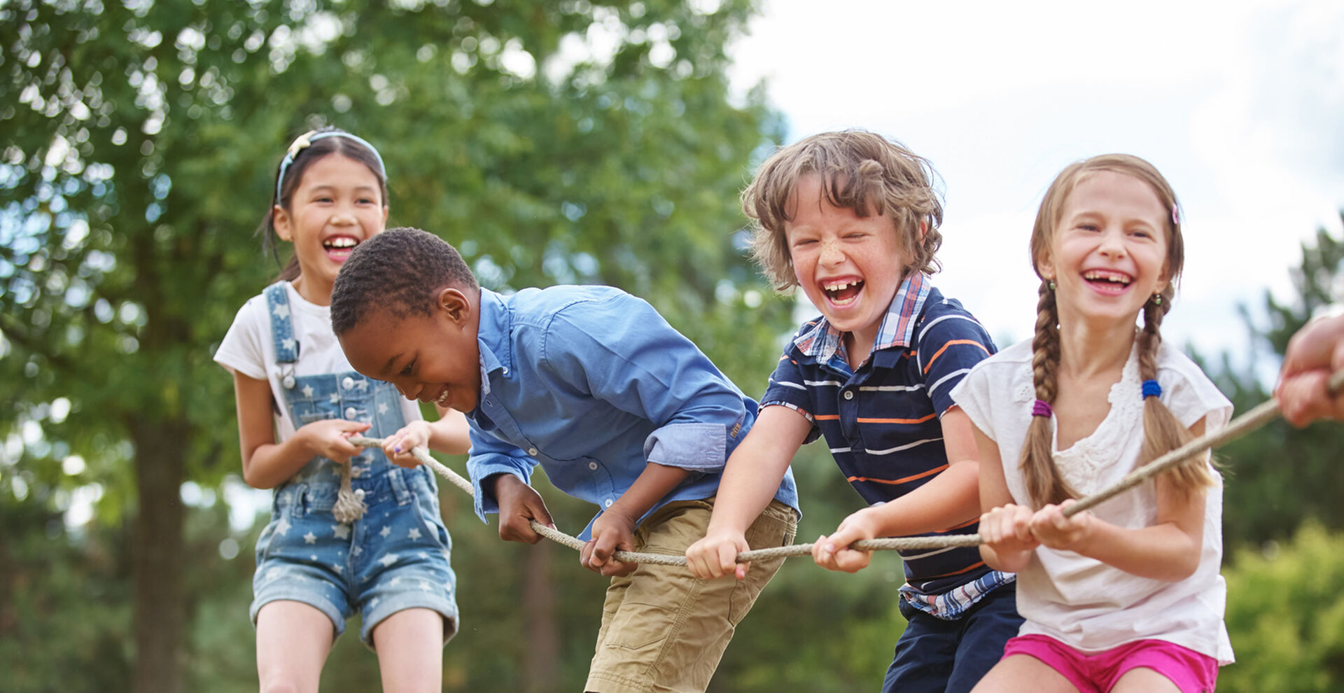 Vier Kinder, zwei Mädchen und zwei Jungs, ziehen lachend an einem Seil.