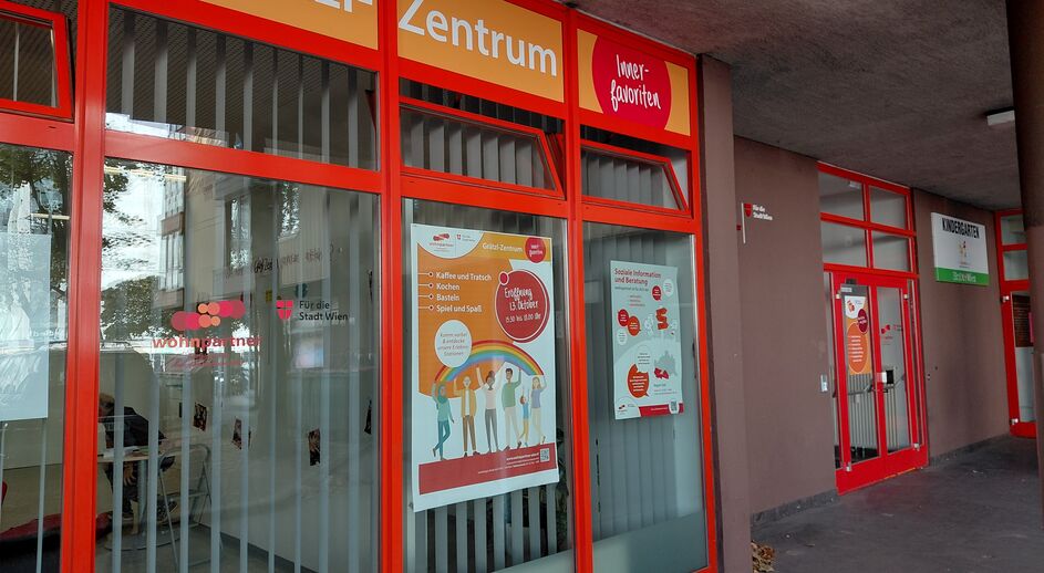 Eingangsbereich eines Grätzl-Zentrums mit orangen Rahmen und Informationsplakaten an den Fenstern