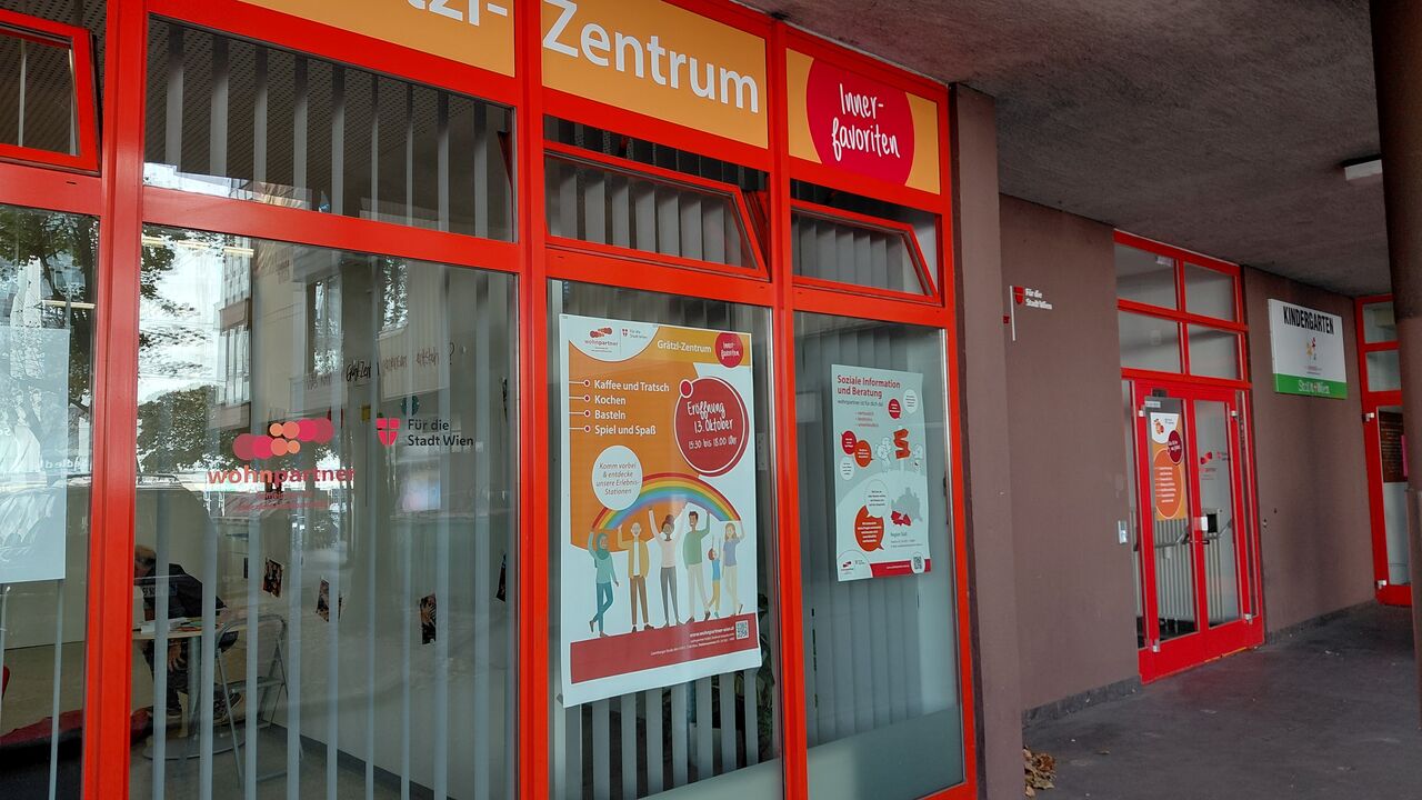 Eingangsbereich eines Grätzl-Zentrums mit orangen Rahmen und Informationsplakaten an den Fenstern