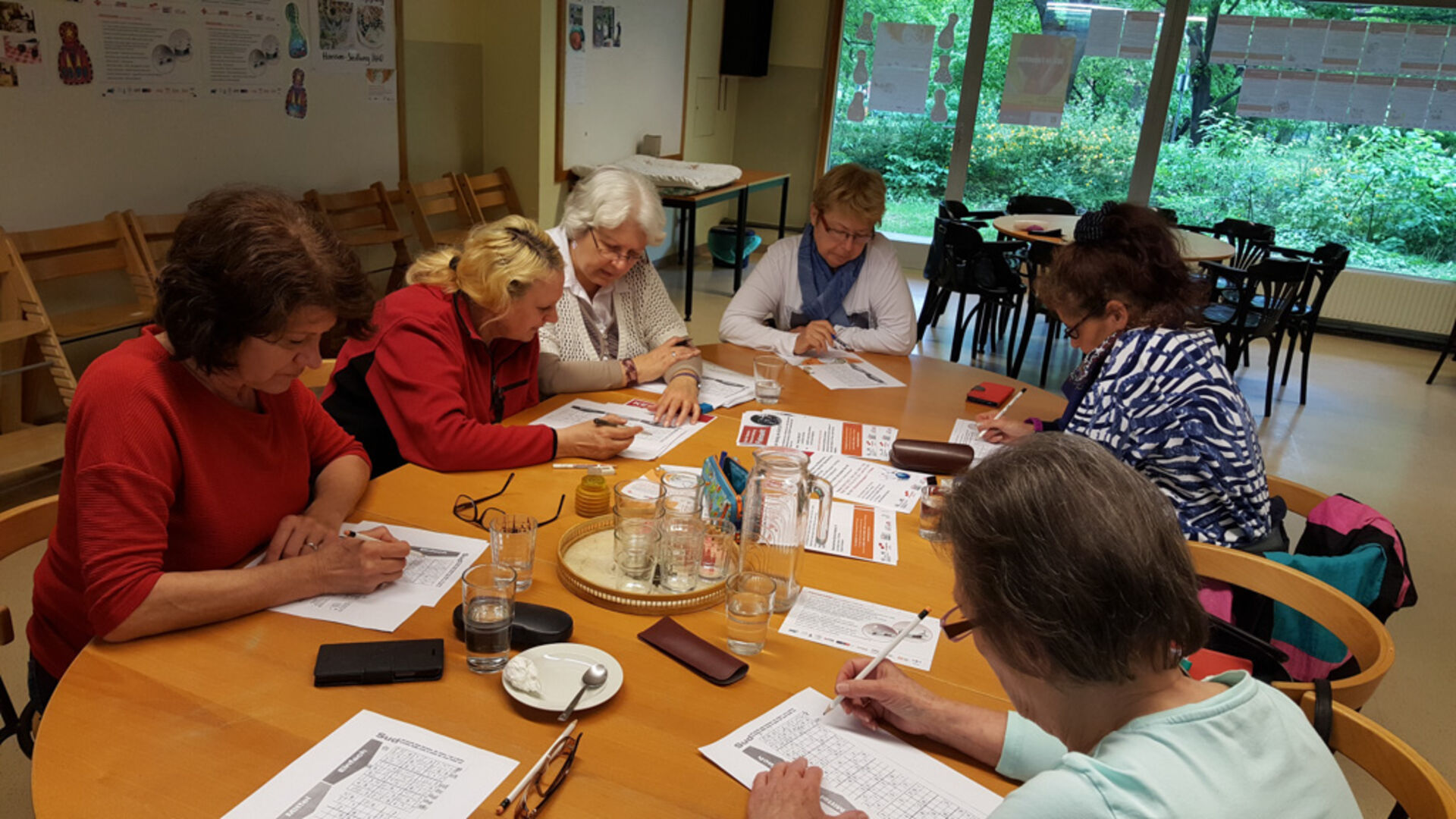 Gruppe Bewohnerinnen und Bewohner am Tisch sitzend und schreibend.