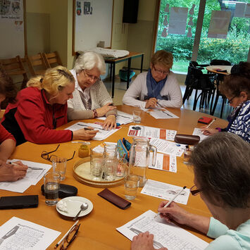 Gruppe Bewohnerinnen und Bewohner am Tisch sitzend und schreibend.