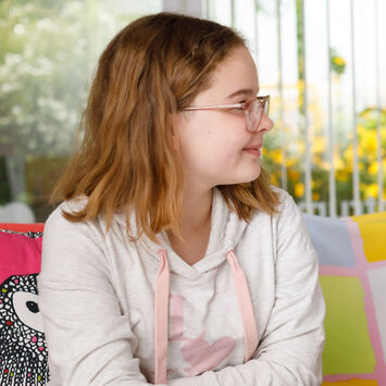 Ein Mädchen erhält Nachhilfe von einem etwas älteren Jungen. Die beiden sitzen an einem Tisch und schauen in ein Schulbuch.