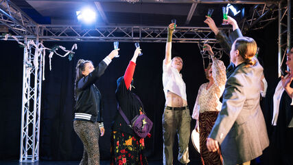 Mehrere Personen stehen im Halbkreis nebeneinander und haben jeweils einen Arm mit einem Sektglas in die Höhe gestreckt. Sie prosten einander zu.