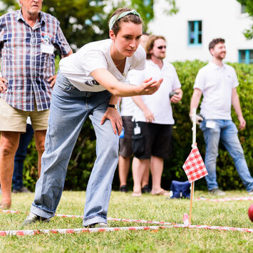 Mehrere Menschen, die auf einem Rasen Boccia spielen.