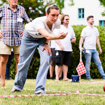 Mehrere Menschen, die auf einem Rasen Boccia spielen.
