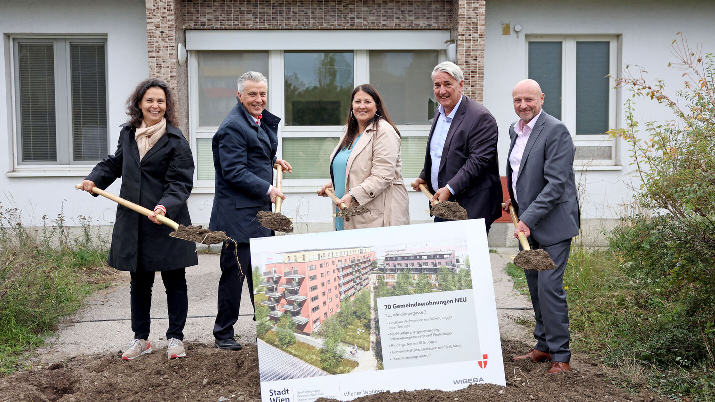 Katharina Klement (Vizedirektorin von Wiener Wohnen), Gemeinderat Josef Taucher, Vizebürgermeisterin und Wohnbaustadträtin Kathrin Gaál, Bezirksvorsteher Ernst Nevrivy und Paul Steurer, Direktor der WIGEBA, stehen jeweils mit einem Spaten voll Erde hinter einer Tafel mit der Visualisierung des Gemeindebau NEU in der Weidingergasse. Sie sind durchwegs herbstlich gekleidet und lächeln in die Kamera. 