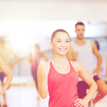 Gruppe von vier jungen Frauen und einem Mann in Sportkleidung beim Training in einem hellen Fitnessraum