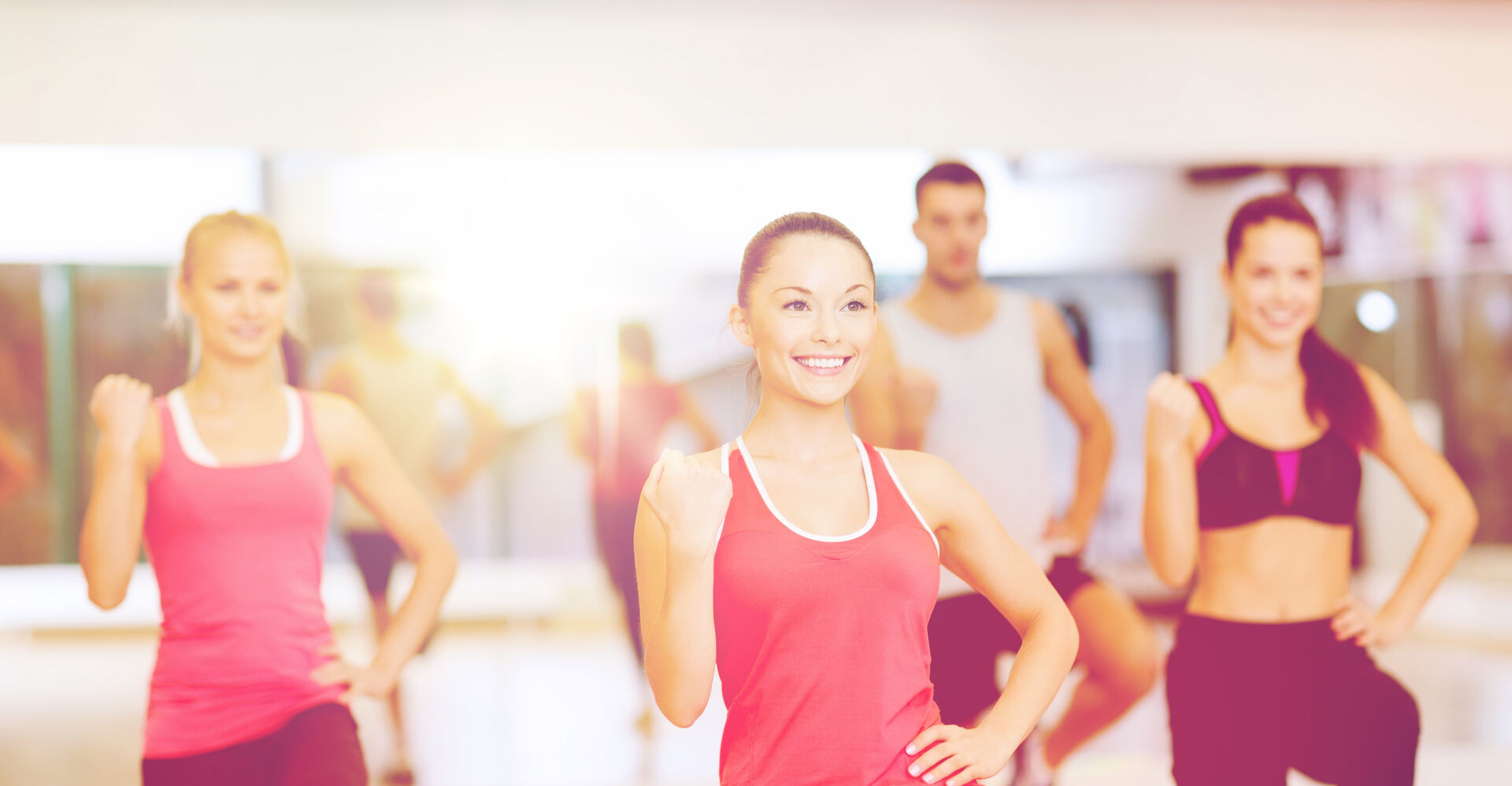 Gruppe von vier jungen Frauen und einem Mann in Sportkleidung beim Training in einem hellen Fitnessraum