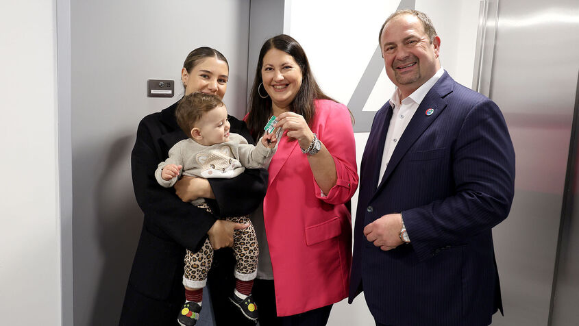 Vizebürgermeisterin und Wohnbaustadträtin Kathrin Gaál und Bezirksvorsteher Alexander Nikolai in der neuen Wohnhausanlage übergeben einer Frau mit Baby am Arm die Schlüssel zu ihrer neuen Wohnung.