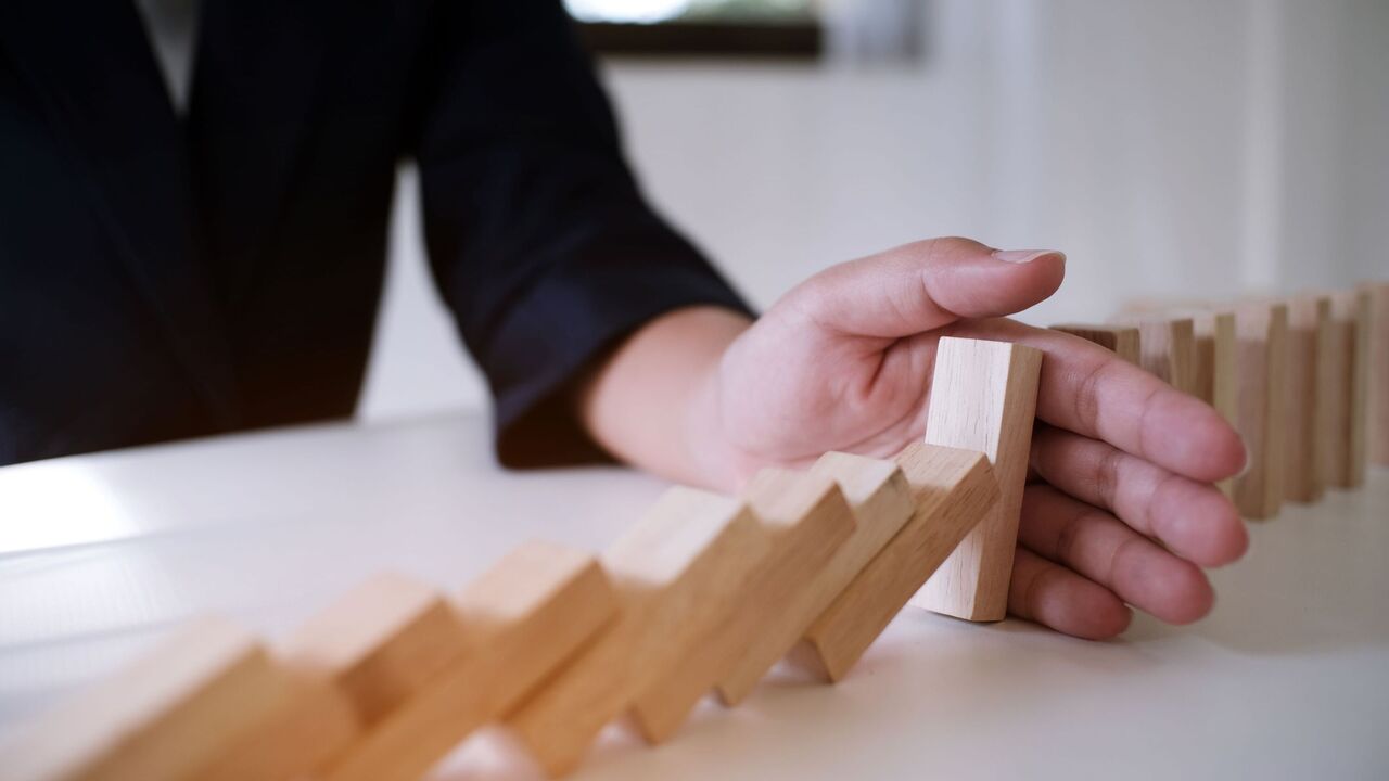 Imagebild: Hand hält eine Reihe fallender Dominosteine auf und symbolisiert damit, dass eine Kettenreaktion unterbrochen wird.