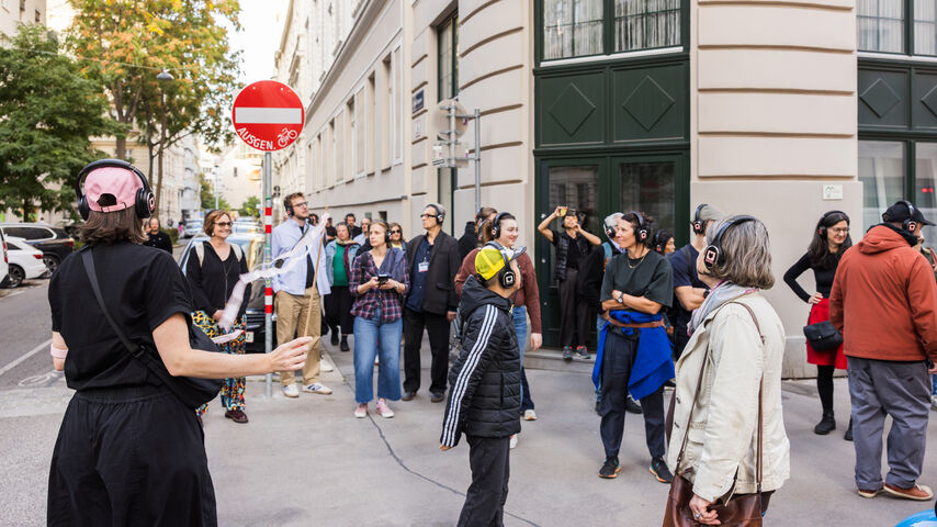 Gruppe von Menschen mit Kopfhörern steht auf einem Bürgersteig in einer Stadtstraße und hört zu