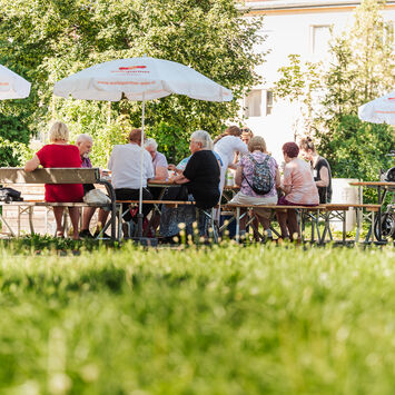 Sommerstimmung im Gemeindebau mit Heurigen-Tischen und -Bänken sowie Sonnenschirmen mit wohnpartner-Logo