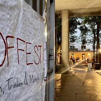 Handgeschriebene Plakatankündigung für ein Hoffest mit Essen, Trinken und Musik an einem Tor mit Blick auf einen beleuchteten Innenhof