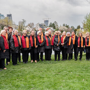 Der 1. Wiener Gemeindebauchor steht mit Chorleiterin Nelli Goncharuk auf einer Wiese und probt.