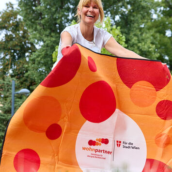 Eine Frau breitet eine Picknickdecke aus, auf der Decke sieht man das wohnpartner-Logo.