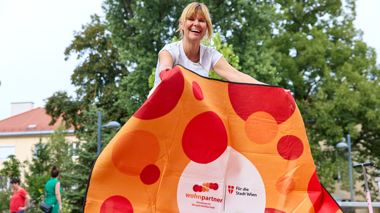 Eine Frau breitet eine Picknickdecke aus, auf der Decke sieht man das wohnpartner-Logo.