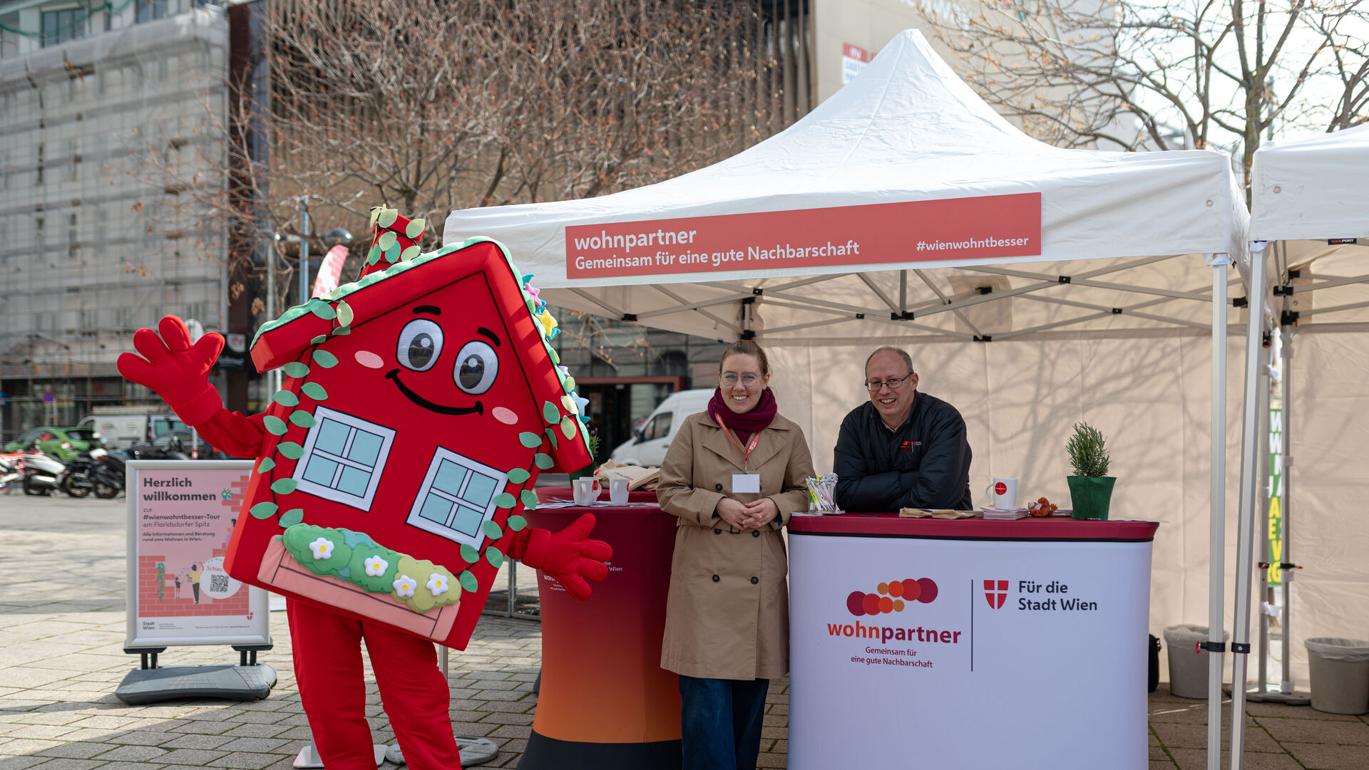 Ein Informationsstand von wohnpartner mit einer Mitarbeiterin, einem Mitarbeiter und dem Maskottchen WohnaLisa