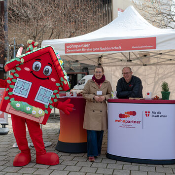 Ein Informationsstand von wohnpartner mit einer Mitarbeiterin, einem Mitarbeiter und dem Maskottchen WohnaLisa
