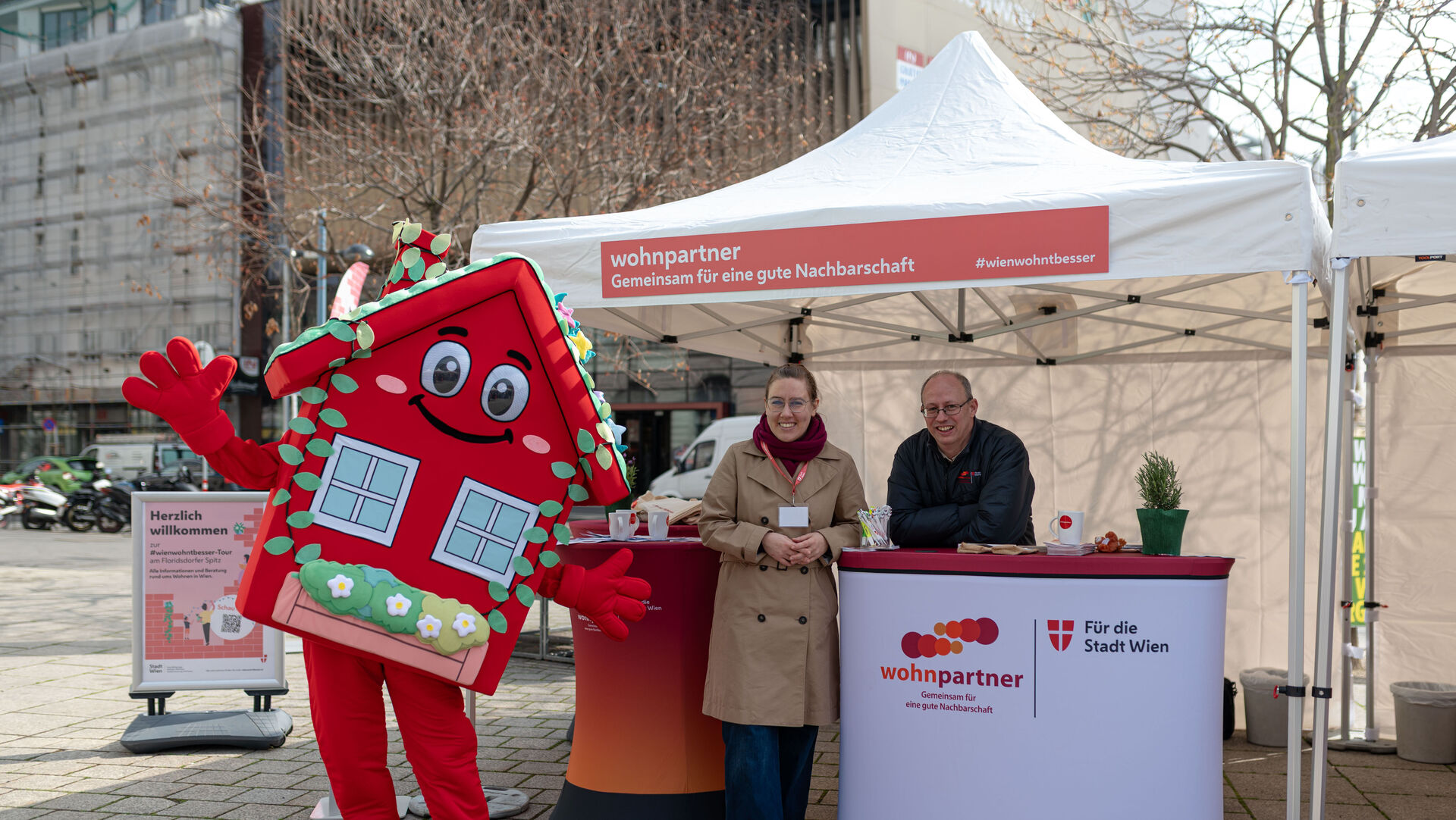 Ein Informationsstand von wohnpartner mit einer Mitarbeiterin, einem Mitarbeiter und dem Maskottchen WohnaLisa