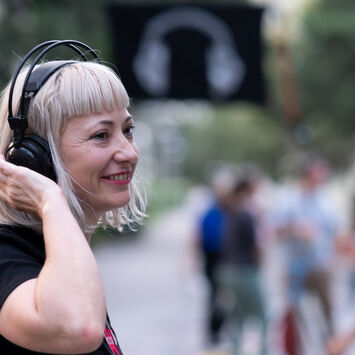 Eine Frau mit schwarzem T-Shirt und Funkkopfhörern bei einer Silent-Disco-Veranstaltung im Freien