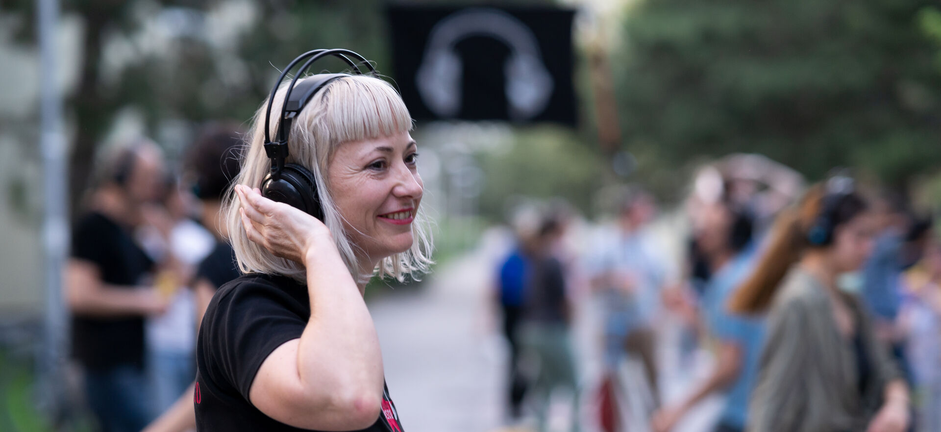 Eine Frau mit schwarzem T-Shirt und Funkkopfhörern bei einer Silent-Disco-Veranstaltung im Freien