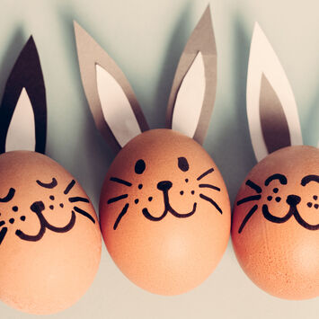 Drei Eier mit aufgemalten Hasengesichtern und aufgeklebten Hasenohren liegen nebeneinander.